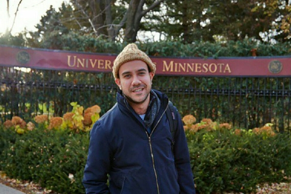 Nico Ramos Flores standing outside, with University of Minnesota sign, trees and bushes in background
