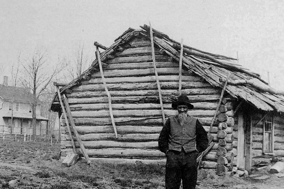 Andrew Peterson in 1885, standing by the log cabin he first lived in on his farm in Waconia. In the background stands the later farmhouse that still exists. Photo: Minnesota Historical Society