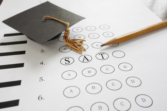 Unfilled test bubbles with the letters "S-A-T" inside. A graduation cap and a pencil on top of the test.