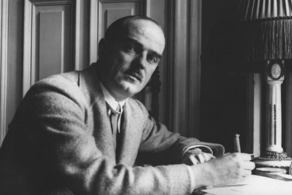 Thorton Wilder in 1931, sitting at a desk with papers and a pen.