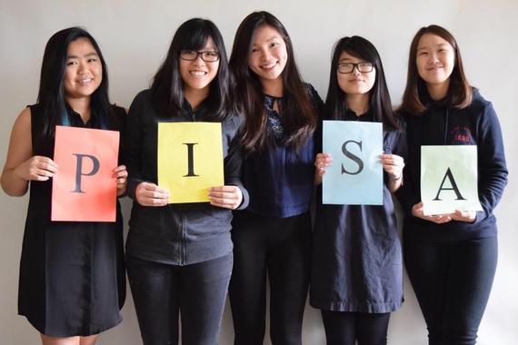 Group of 5 young women. Four of them hold up papers with the letters P, I, S, A printed on them to spell PISA