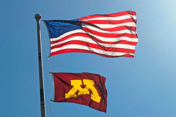 Photo of a flagpole with the flag of the United States flying above a flag with the University of Minnesota Block M against a clear blue sky