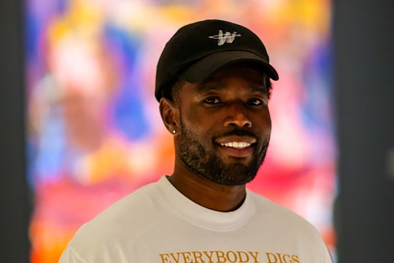 Smiling Black man in baseball hat and tshirt in front of colorful artwork