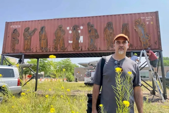 Man stands in front of a raised storage container with metal cutouts of people attached.