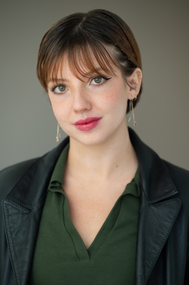 A person with bangs and hair pulled back smiles softly at the camera, wearing a green shirt and pink lipstick.