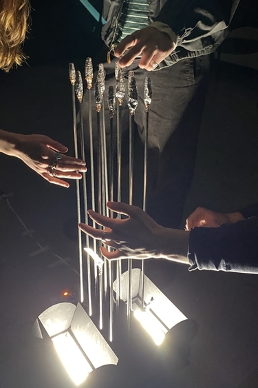 Three undergraduate students touching a sonic instrument's thin metal poles 