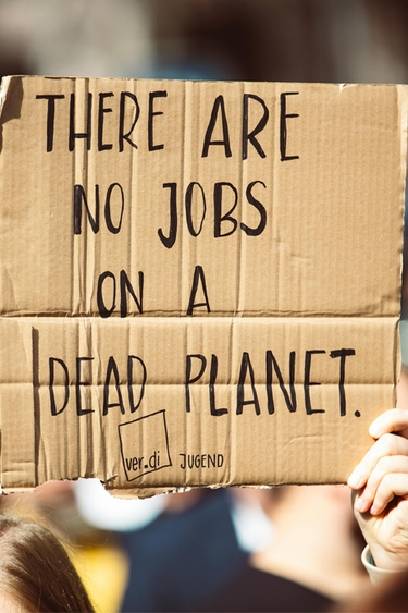 White hand holding cardboard sign that reads "THERE ARE NO JOBS ON A DEAD PLANET."