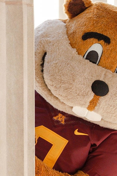 Goldy Gopher peering out from behind column