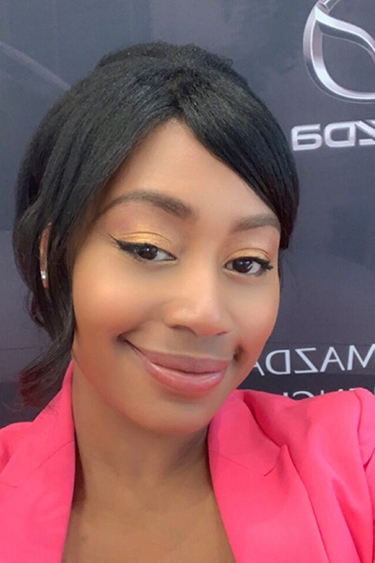 Head and shoulders of person with dark hair pulled back, brown skin, smiling and wearing pink suit