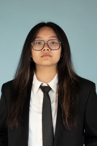 Image of a young person with glasses, long hair, wearing a suit looking ahead.