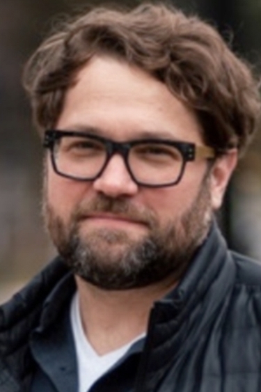 White man with brown hair and beard and glasses with chunky dark frames