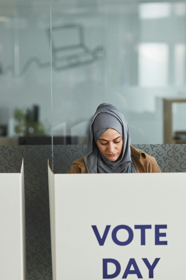 A woman wearing a hijab votes behind a white voting privacy shield