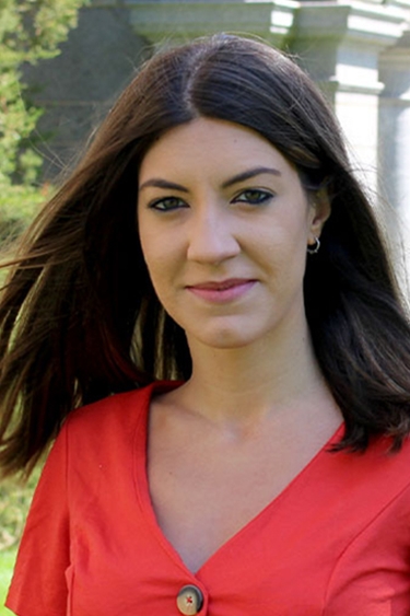 Celia Bravo Díaz, a person with long dark brown hair, wearing a vermillion colored v-neck top