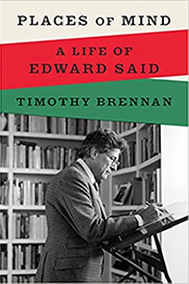 Cover image of Places of Mind with text over three broad swathes of white, red, and green in top 1/3 and bottom 2/3 a black and white photo of Said writing at writing stand in front of bookshelves