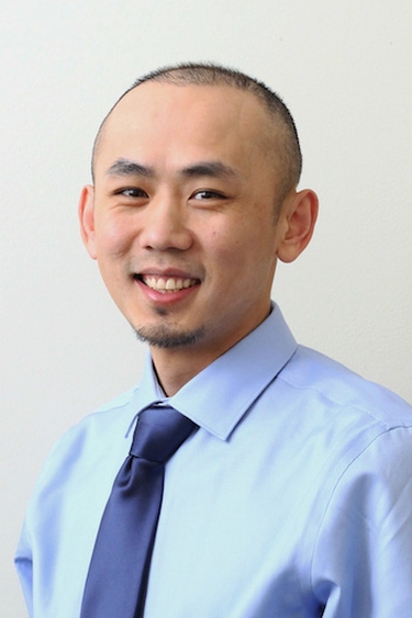 Pao Moua, a person with light skin, dark short hair and a beard, wearing a light blue buttoned shirt and blue tie