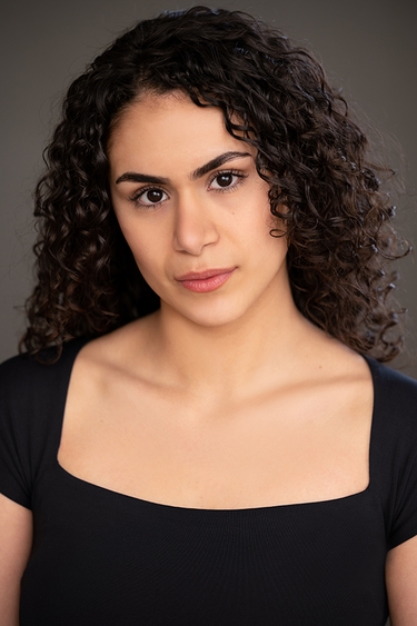 Female Actor with a black top, looking into camera confidently.