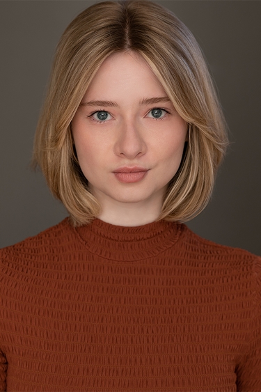 Female Actor wearing a red mock-turtleneck looking into camera confidently.