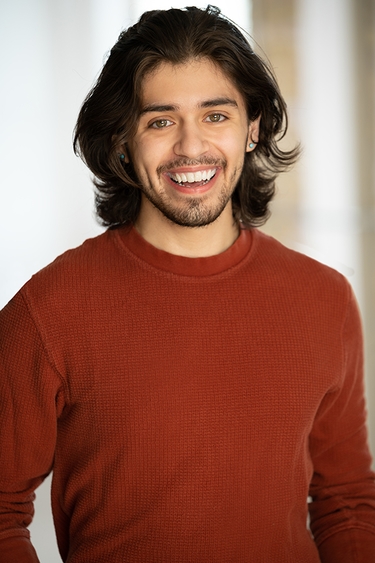 Male Actor in a red long sleeve shirt looking into camera confidently with a smile.
