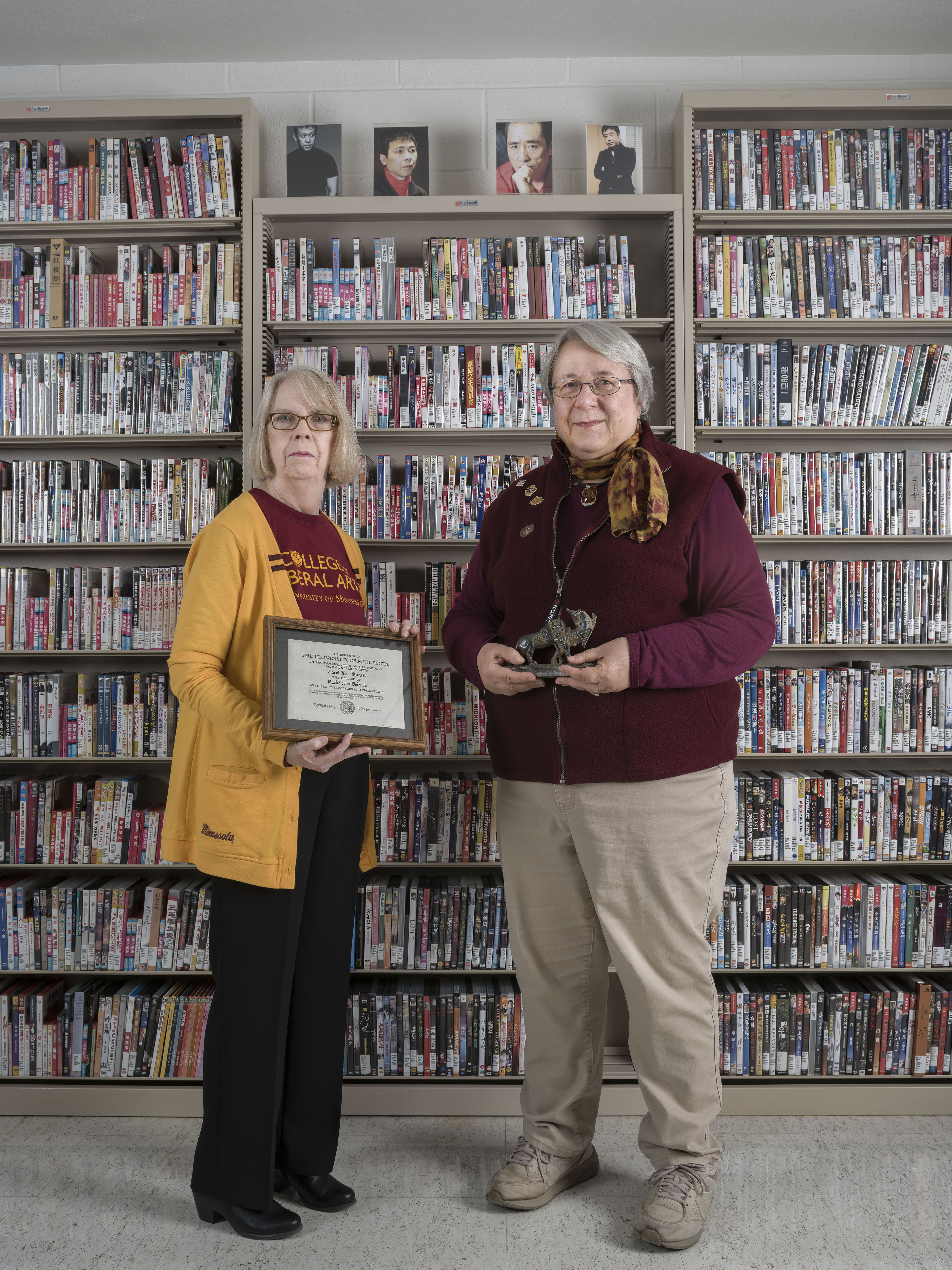 Two Alumnae stand in the East Asian library holding personal artifacts.