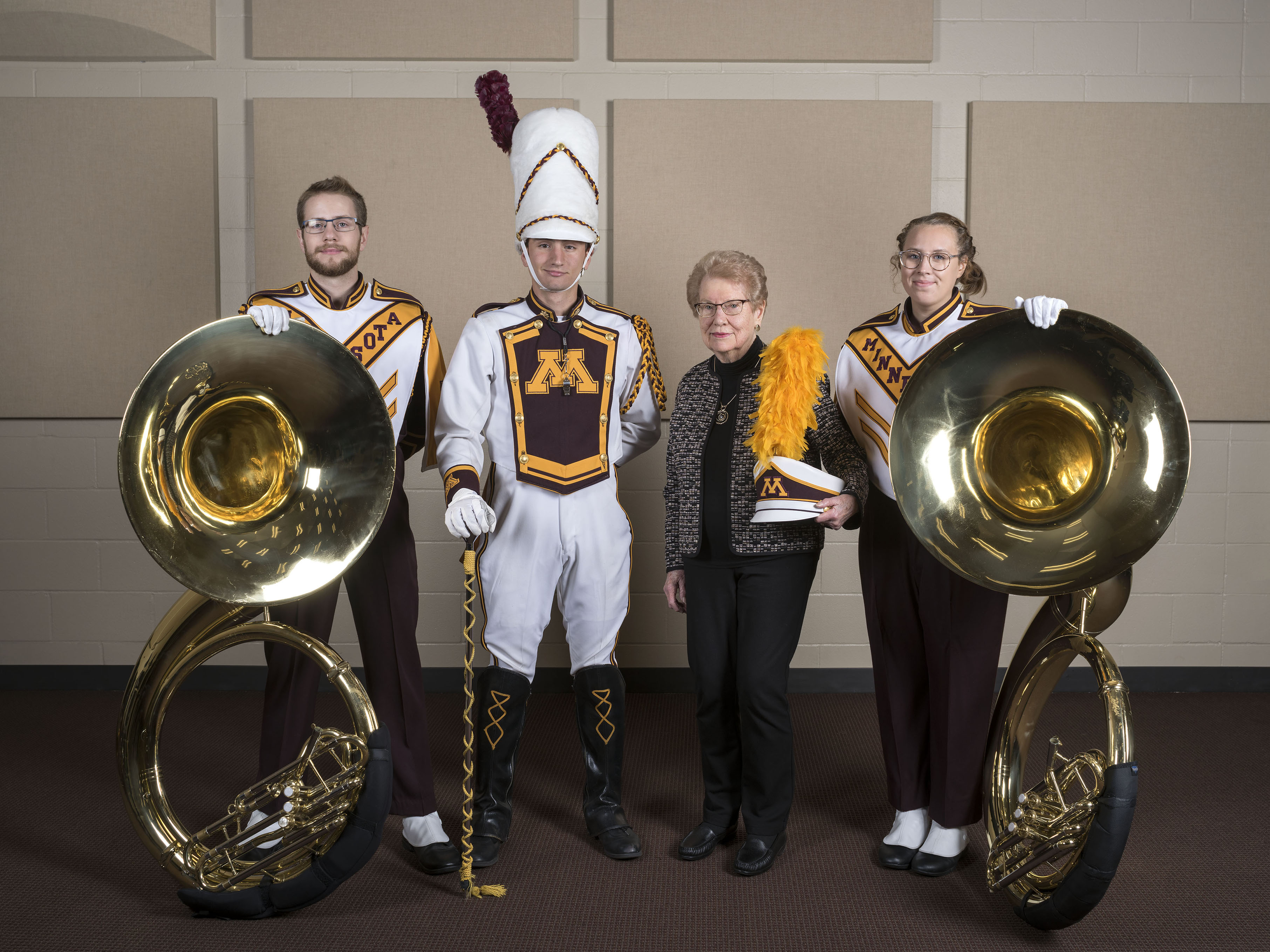 Two tuba players, drum major and Jean Holten in a band practice room.