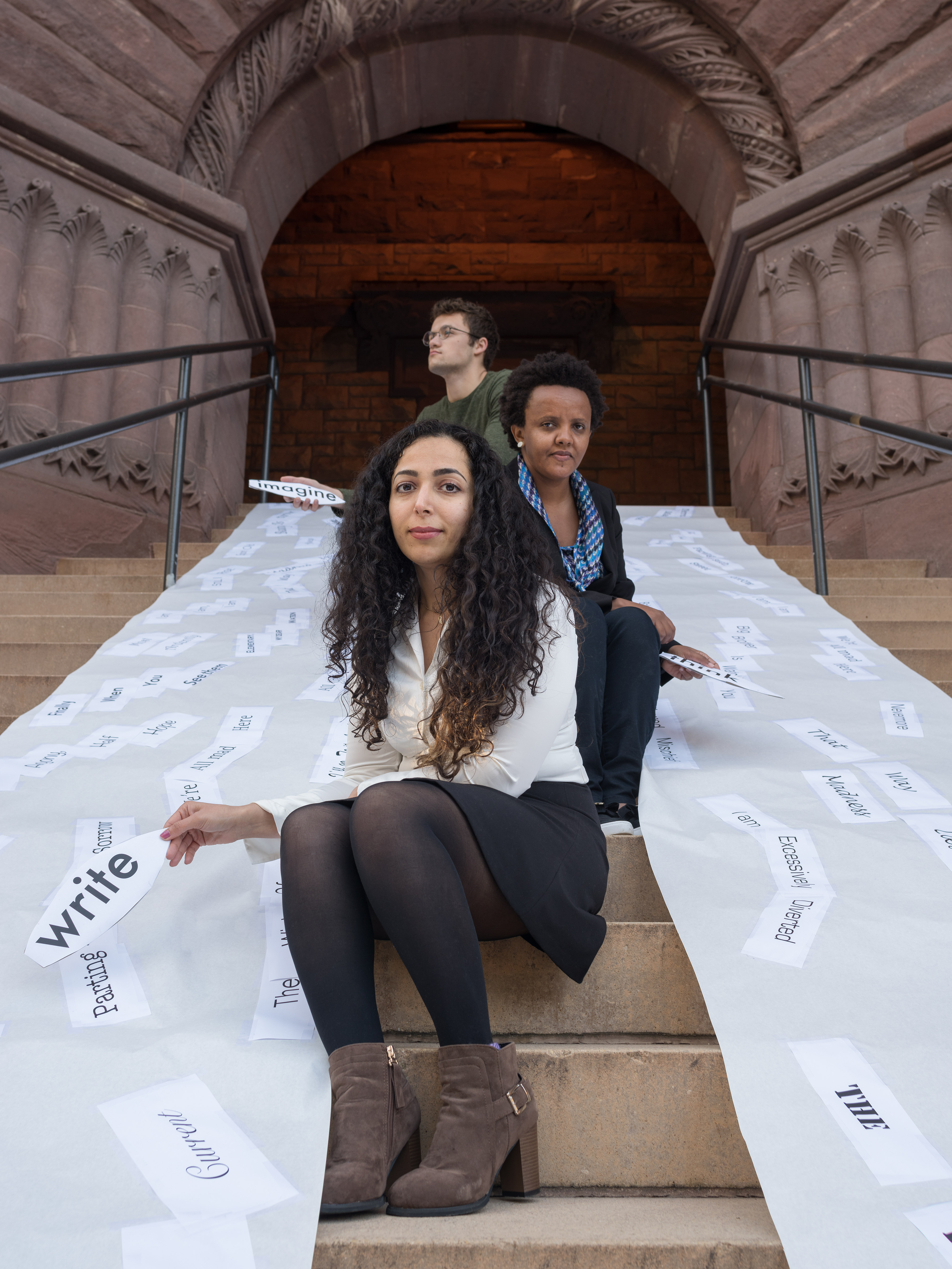 Three Students seated in front of Pillsbury hall in a sea of words.