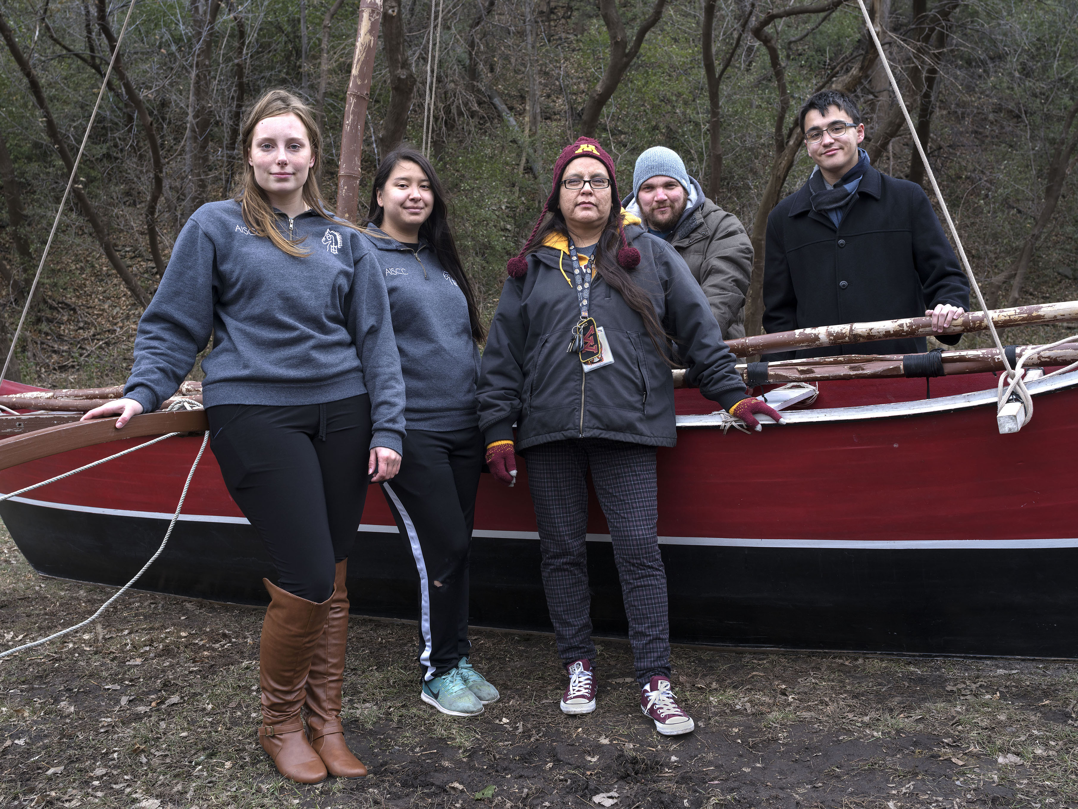 Five students stand around a large traditional ocean fishing boat.