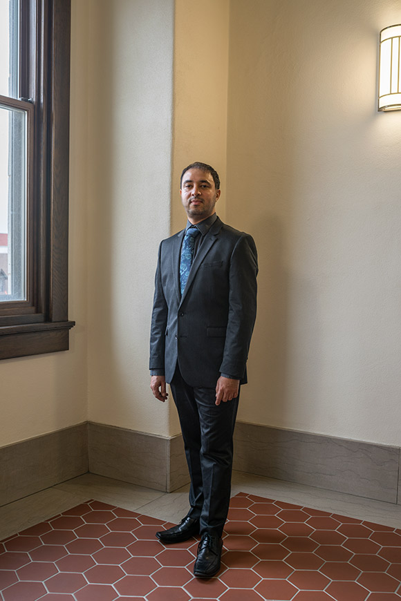 Portrait: Hakim Abderrezak wearing a suit, standing near a window in Folwell Hall
