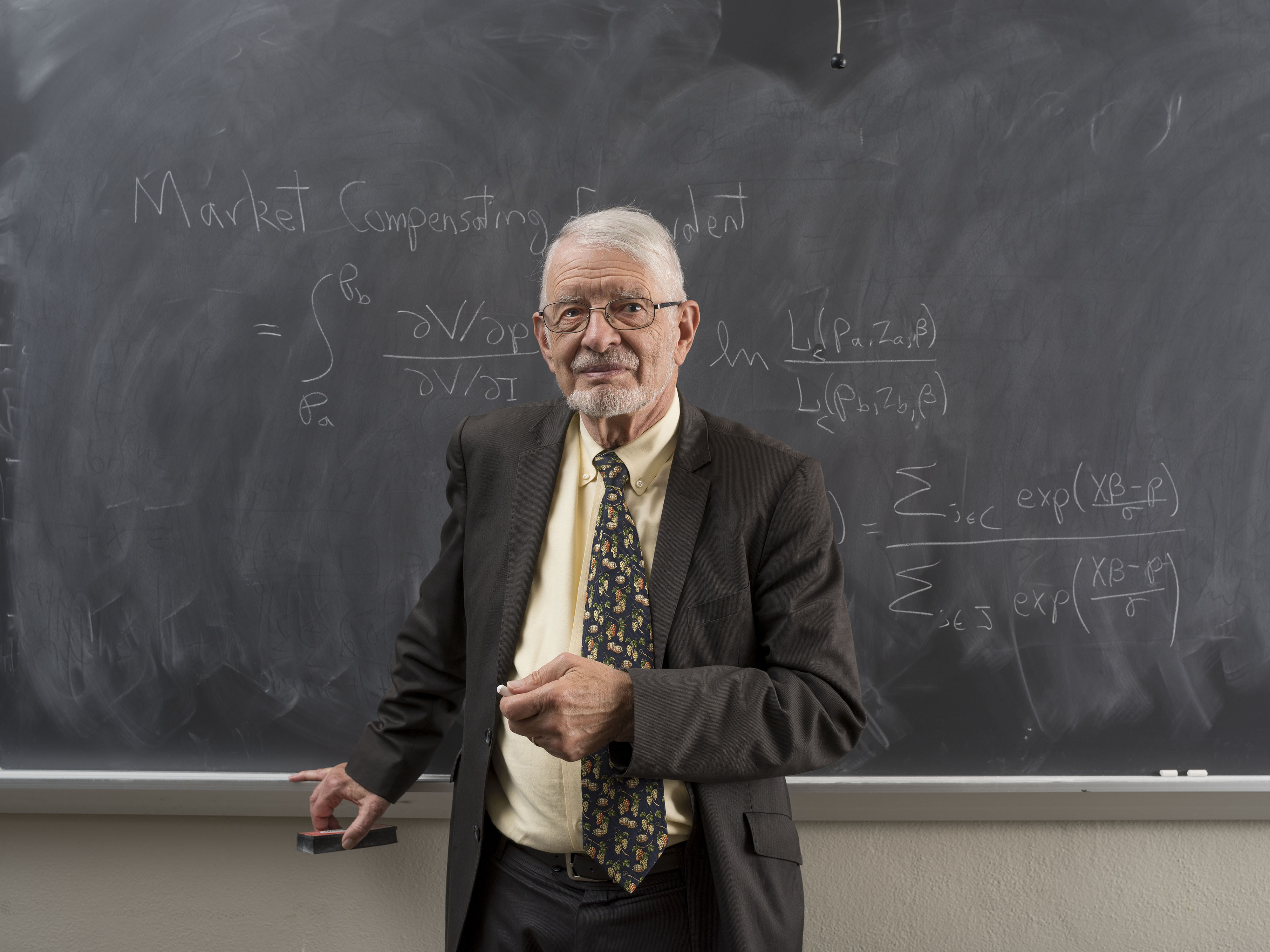 Daniel McFadden standing in front of a chalk board with an equation written on it.