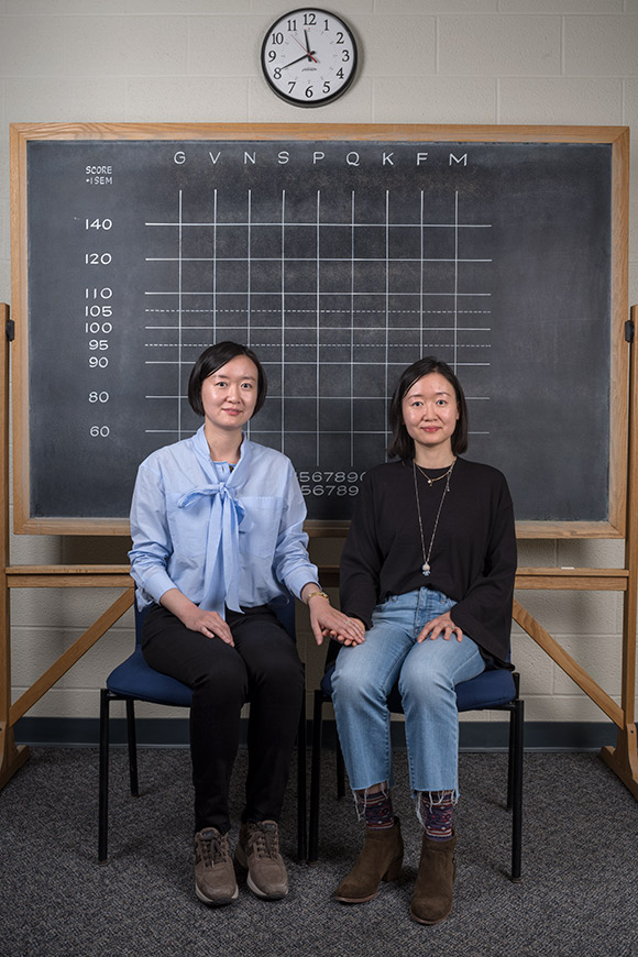 Li Wang, and Chun Wang sitting in front of a blackboard, hand in hand