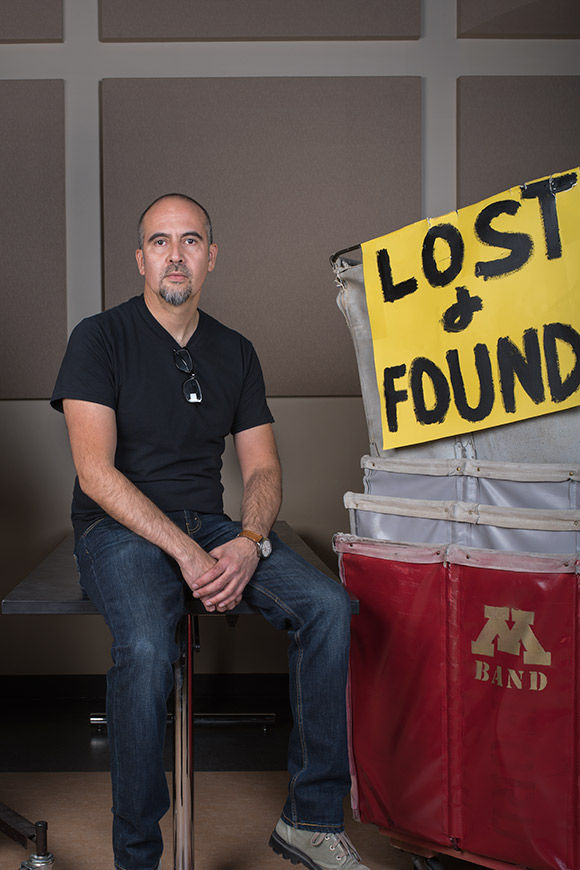 Photo of photographer Xavier Tavera sitting on a stool next to some bins and a Lost and Found sign