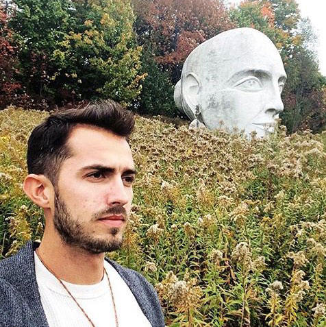 Joey Heinen standing in a garden near a statue of a head.