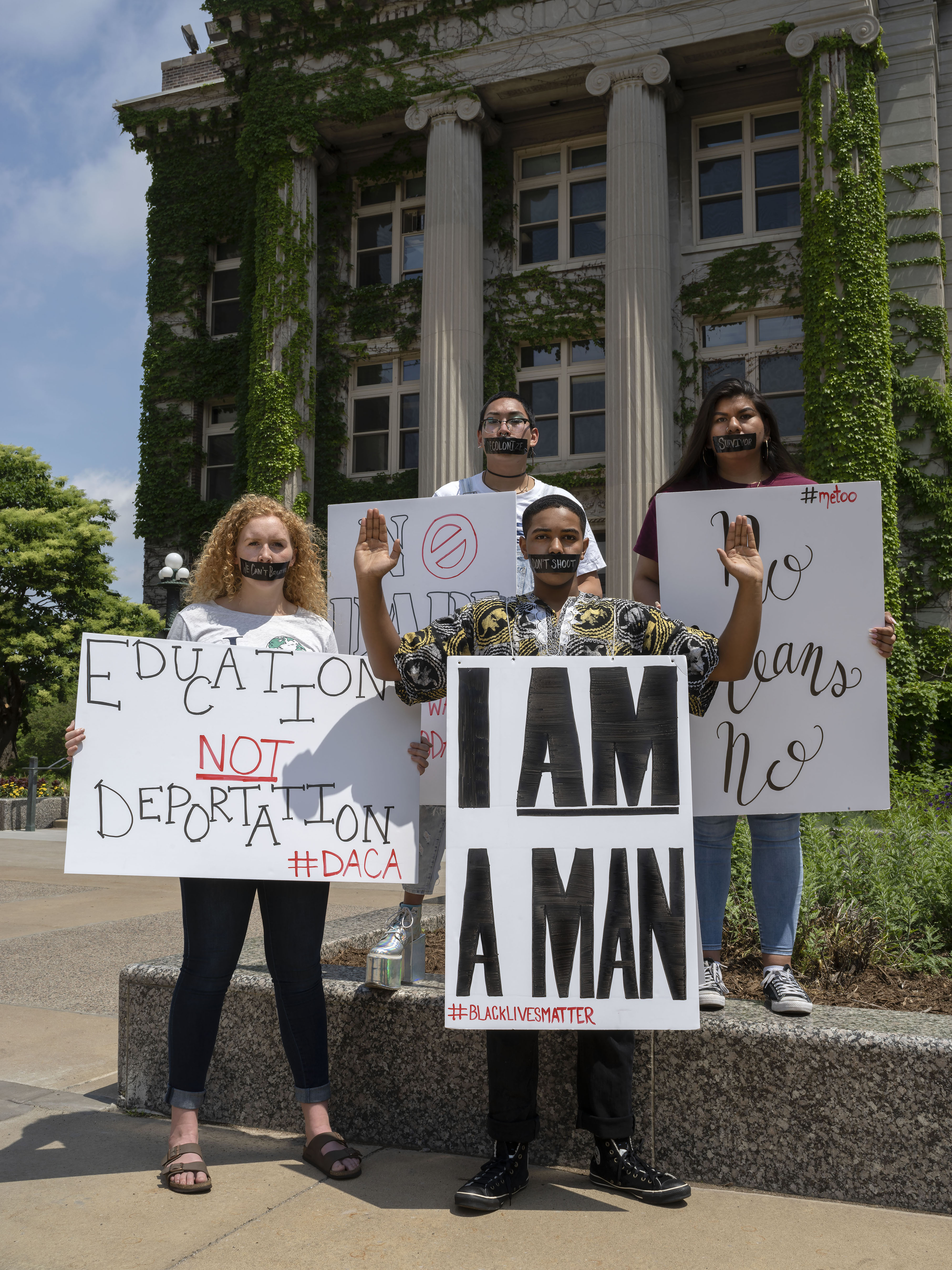 Four students stand with protest signs relevant to 2018 social causes in front of Morrill Hall