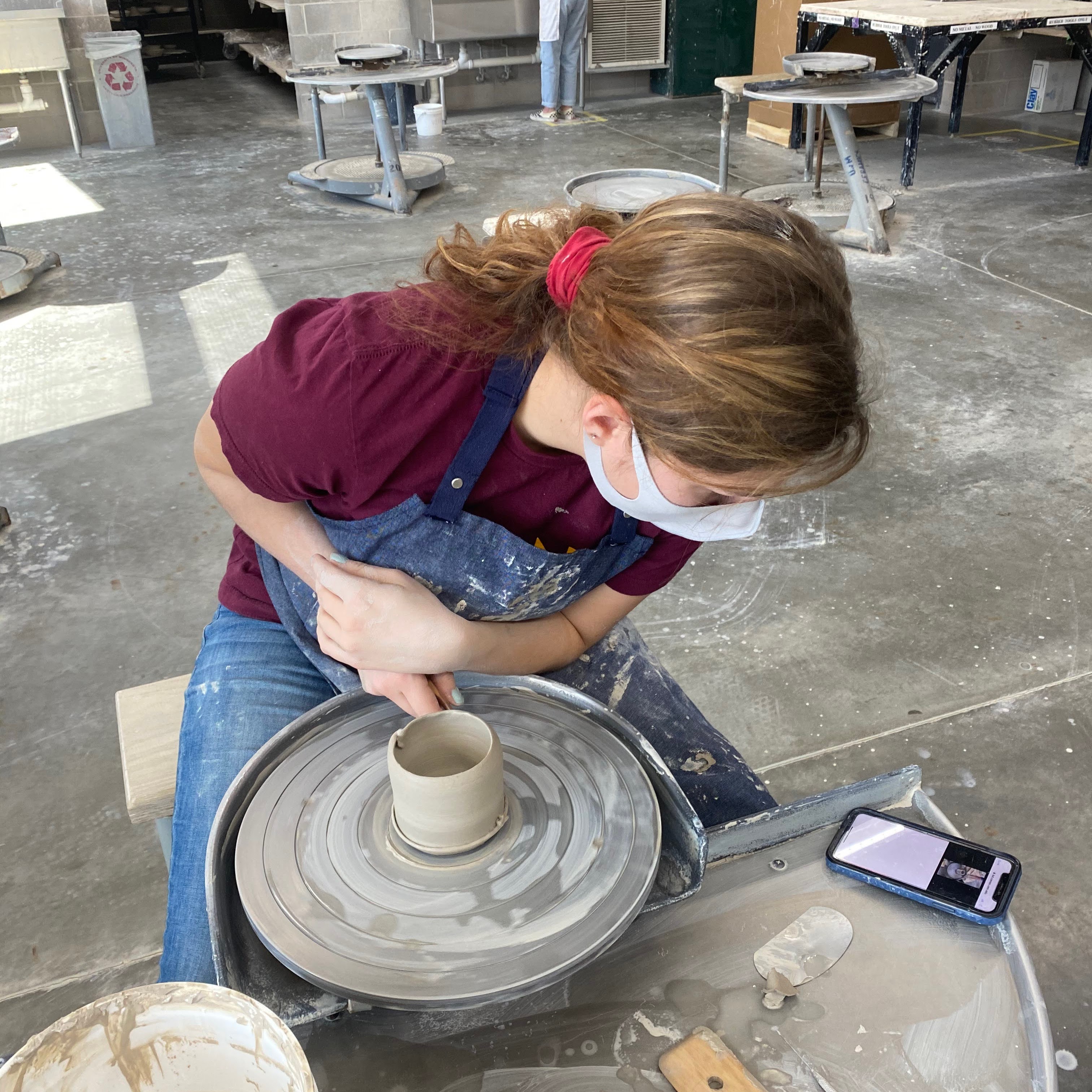 Student at ceramics wheel watching video demo on their phone