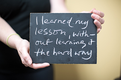 Photo of hands holding sign "I learned my lesson without learning it the hard way."