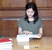 Image of PhD candidate Eunkyung Cho at desk looking at book