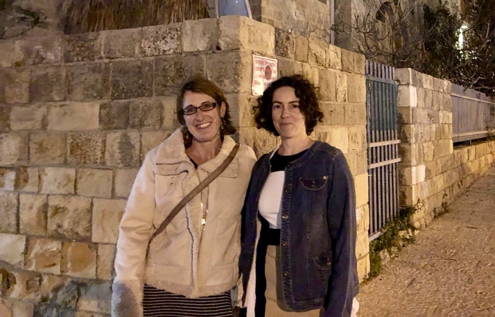 Two women stand on a stone street in front of an old stone building in Israel