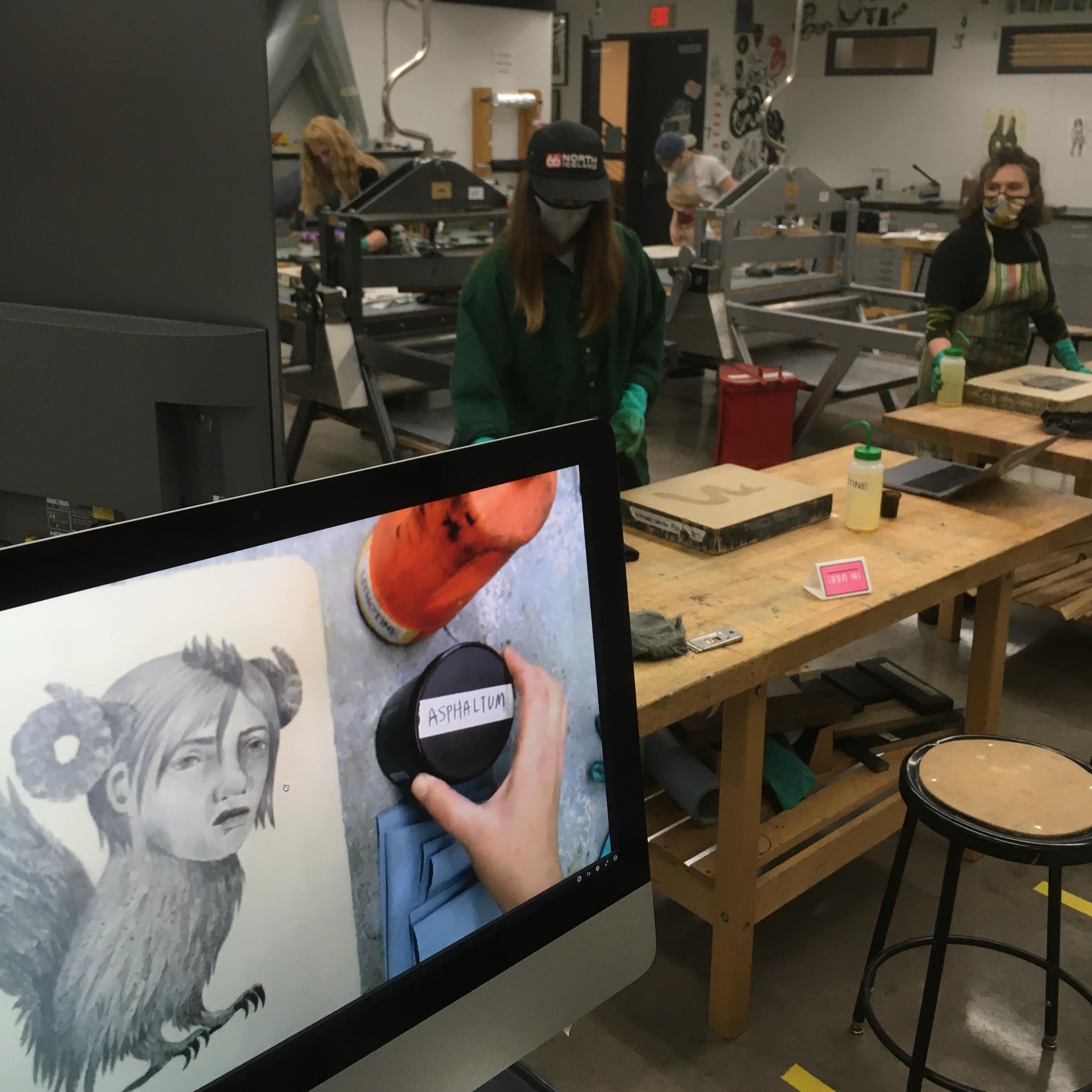 students work in the printmaking studio watching a monitor showing techniques