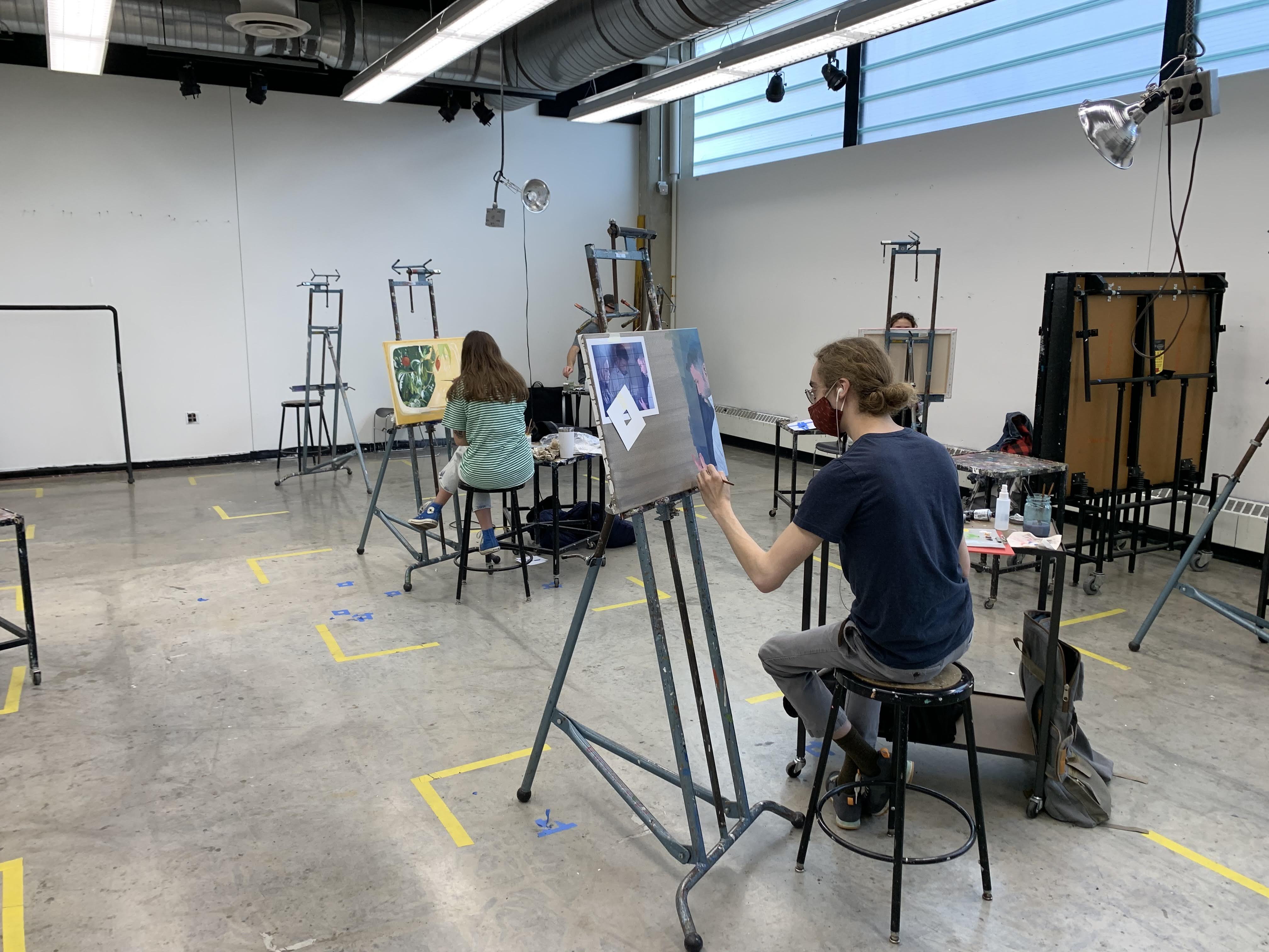 Students painting on spaced out easels in painting studio