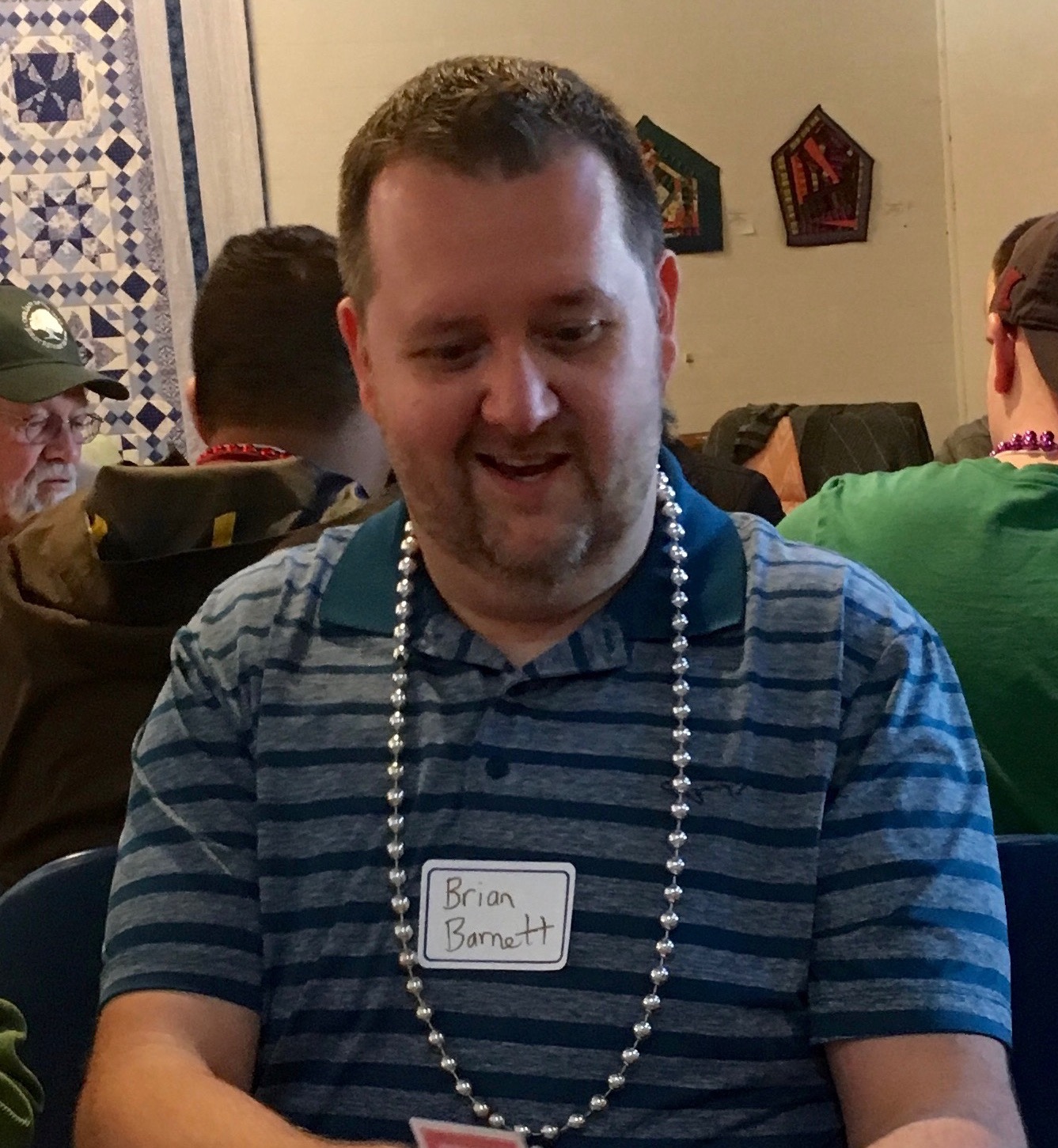 Picture of Brian Barnett sitting at a table with playing cards in his hands with a nametag in the center of his chest and a 