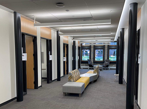 Photo of hallway with yellow and grey couch in middle and offices to right and left