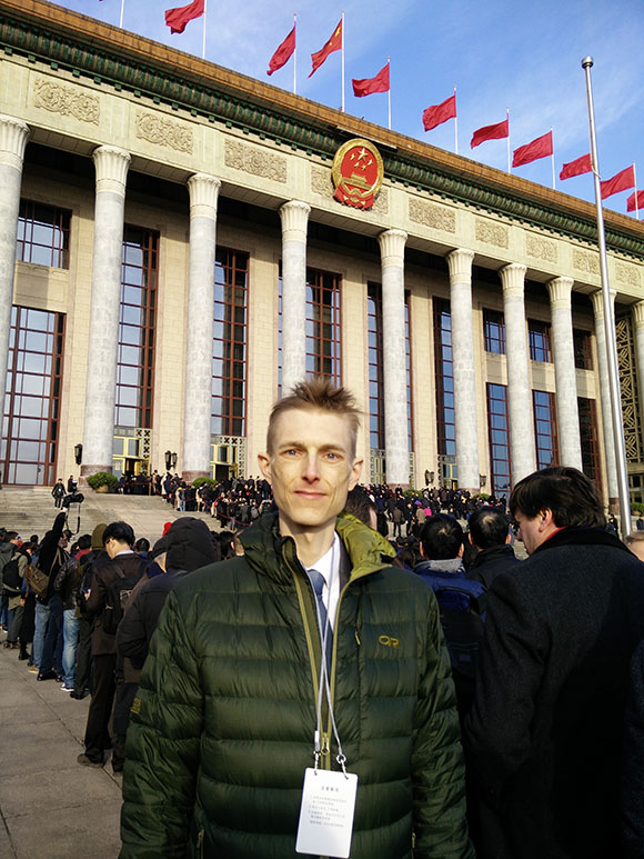 Man standing in front of crowd on the steps of the Great Hall of the People in Beijing, China.