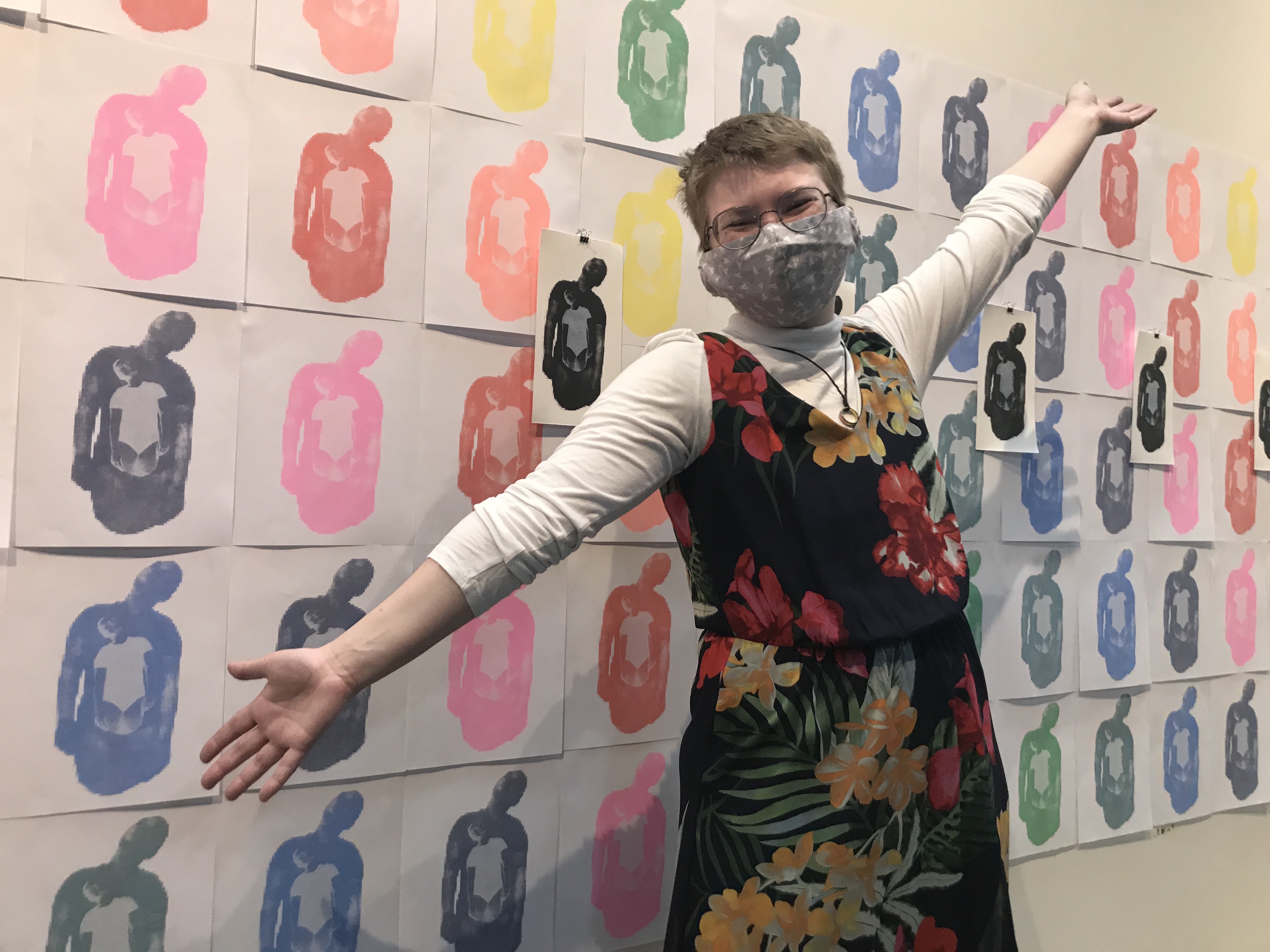 smiling masked student standing in front of their print installation