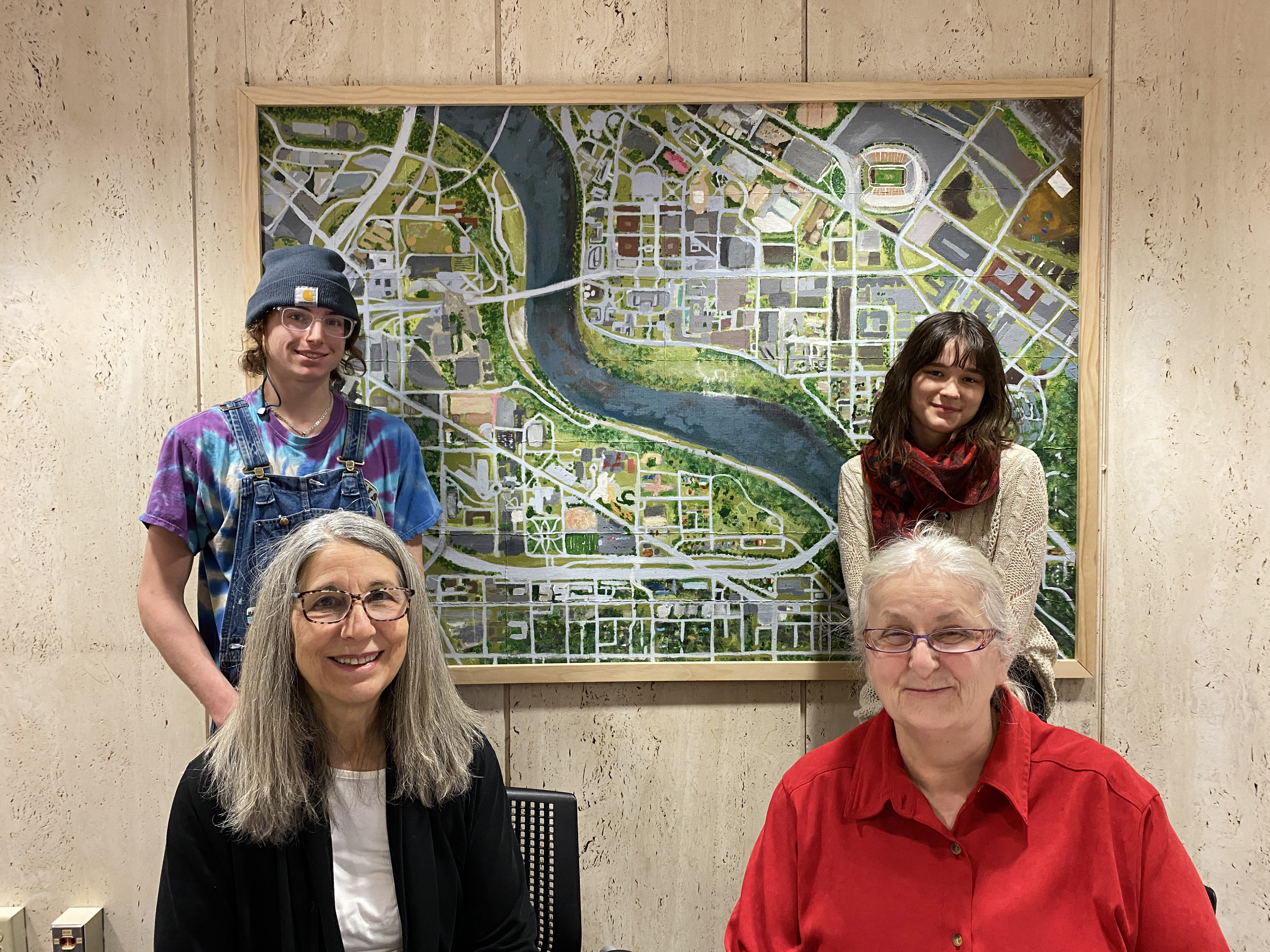 Four students stand and sit in front of a large framed map